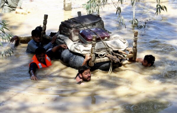 Displaced people float belongings salvaged from flood-hit homes through a flooded area, on the outskirts of Peshawar, Pakistan, Sunday, Aug. 28, 2022. Officials in Pakistan say deaths from widespread flooding have topped 1,000 since mid-June. Flash flooding from the heavy rains has washed away villages and crops as soldiers and rescue workers evacuated stranded residents to the safety of relief camps and provided food to thousands of displaced Pakistanis. (AP Photo/Mohammad Sajjad)